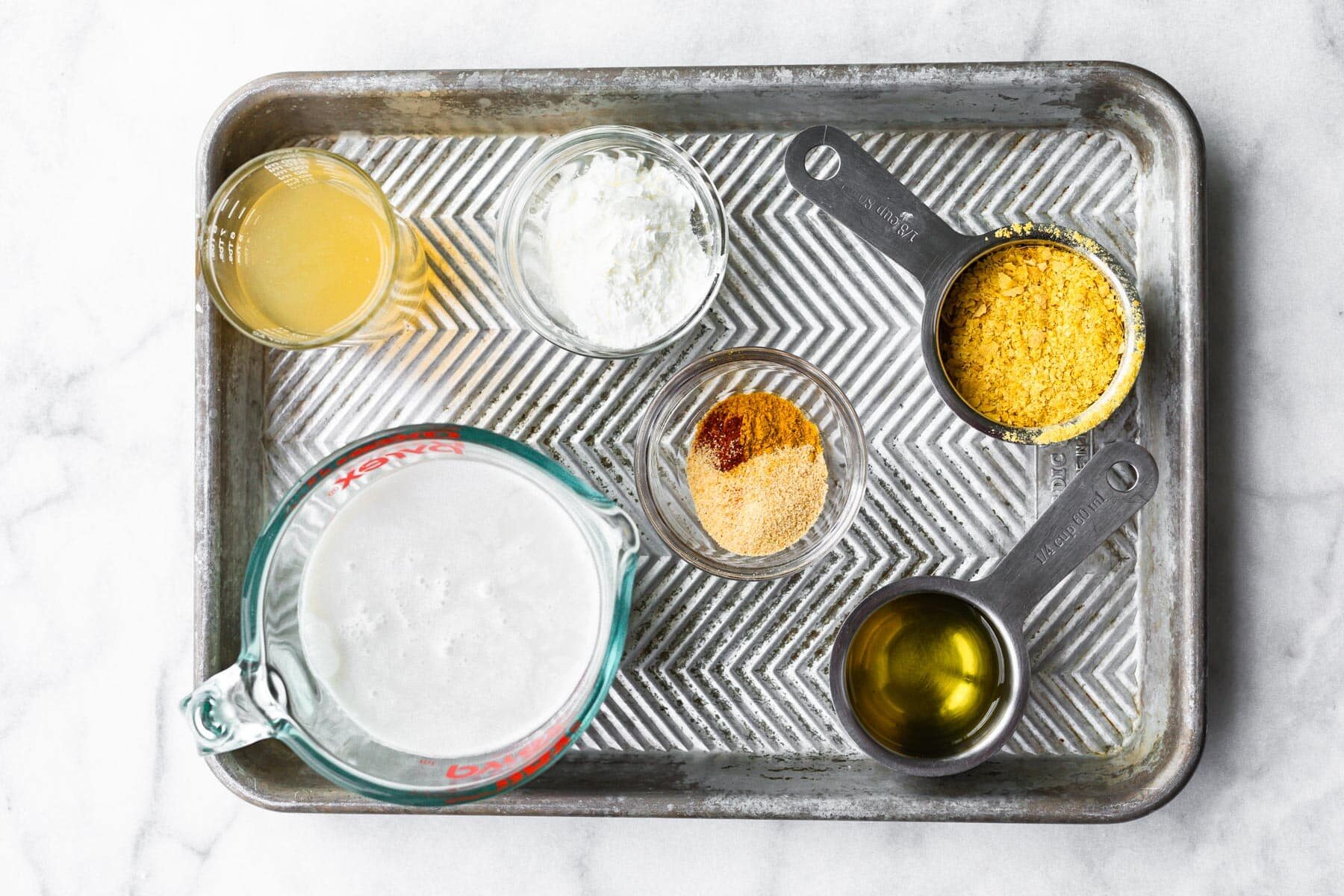 Bowls of ingredients to make vegan cheese sauce on a metal baking sheet.