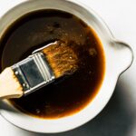 A brush dipped into a bowl of low sugar maple bourbon glaze.