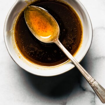 A spoon with maple bourbon glaze over a bowl of low sugar glaze.