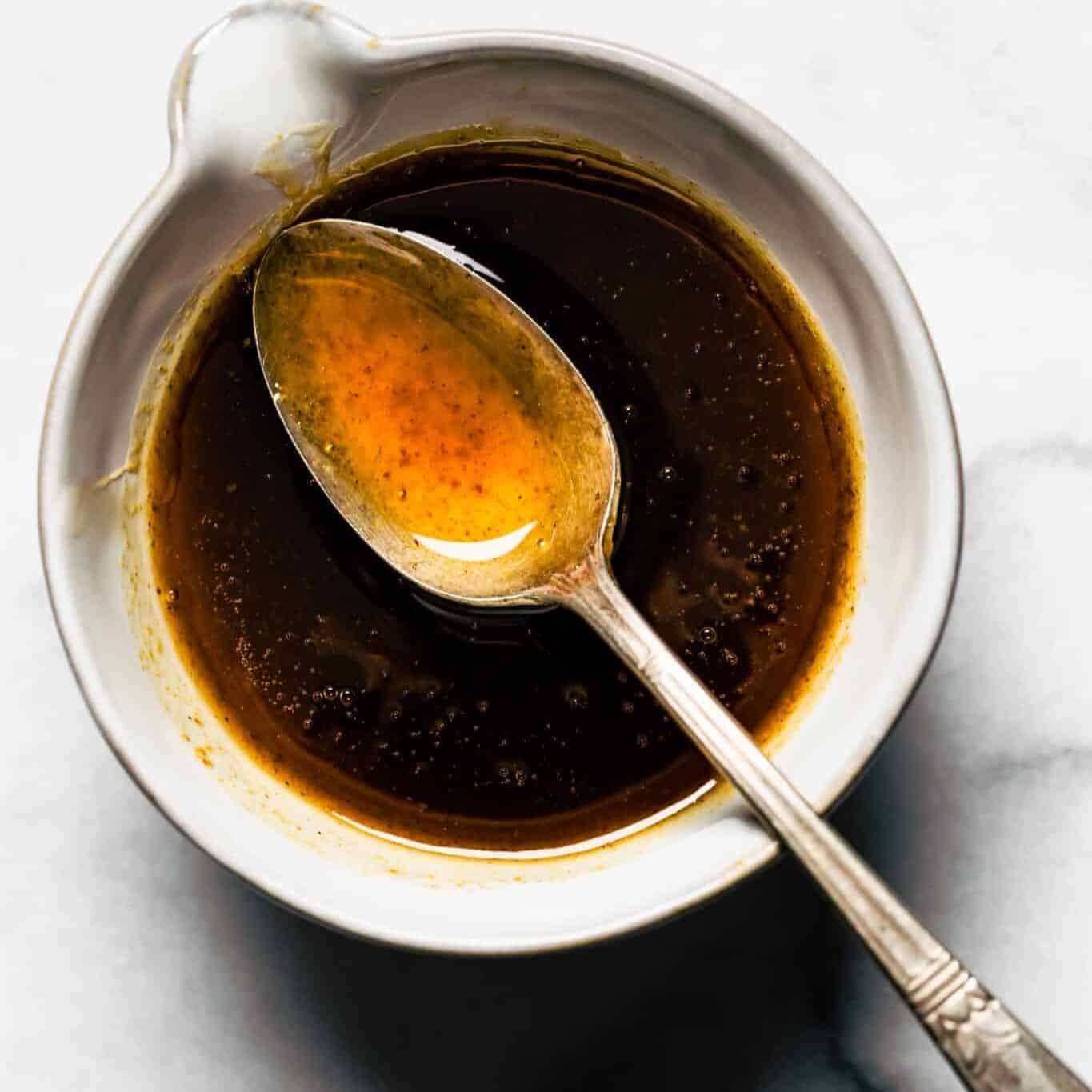 A spoon with maple bourbon glaze over a bowl of low sugar glaze.
