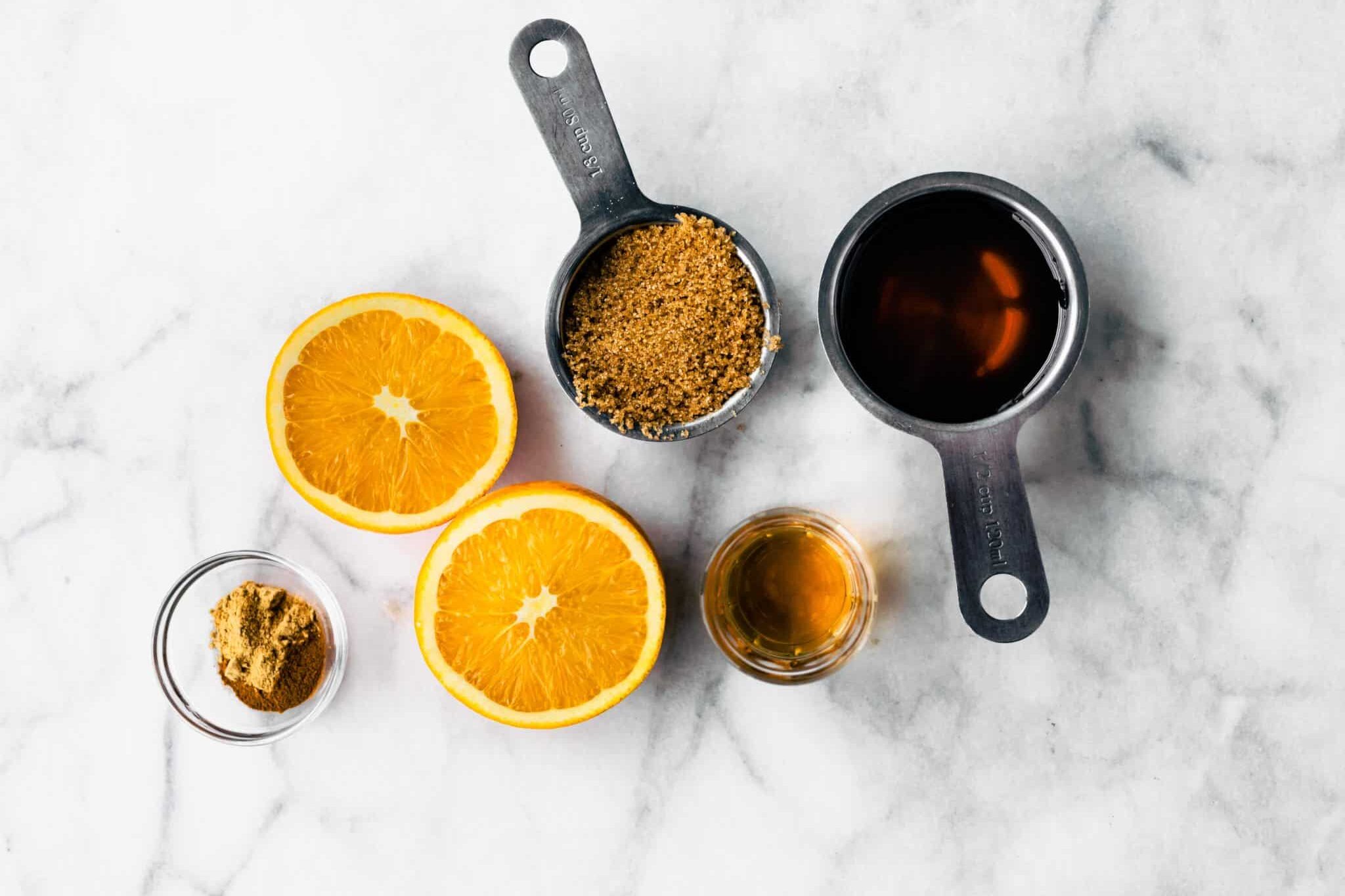 Measuring cups filled with coconut sugar and maple syrup and fresh oranges on a countertop.