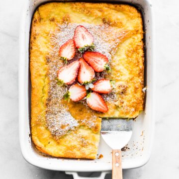 A gluten free Swedish Pancake topped with sliced strawberries and a slice removed.