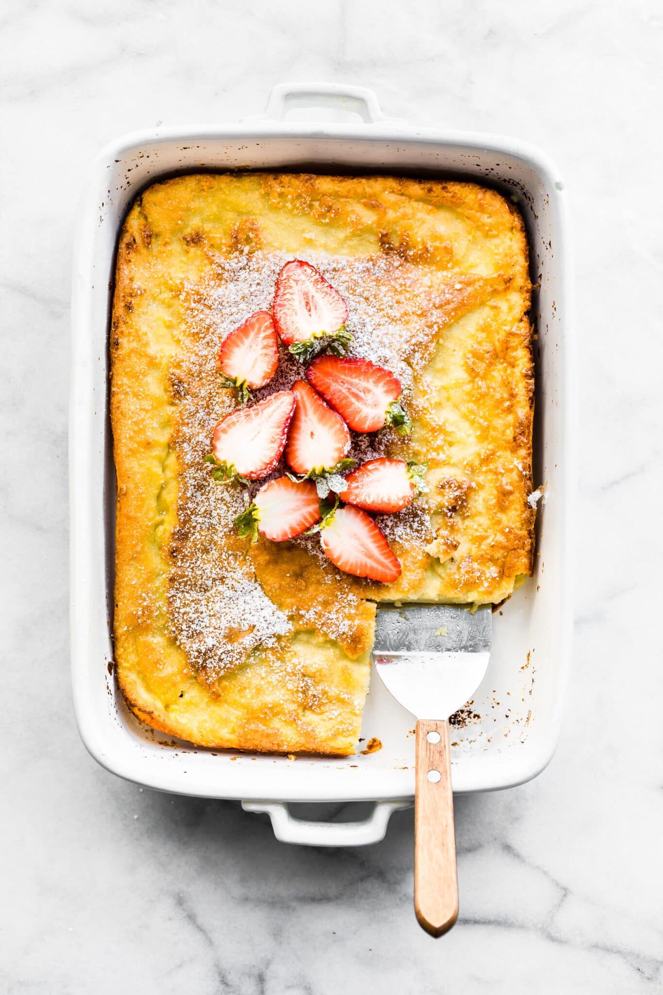 A gluten free Swedish Pancake topped with sliced strawberries and a slice removed.