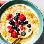 A woman holding a bowl of AIP breakfast porridge topped with berries and cream.