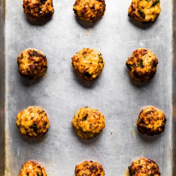 Overhead photo of twelve cooked gluten free chicken meatballs on a sheet pan.