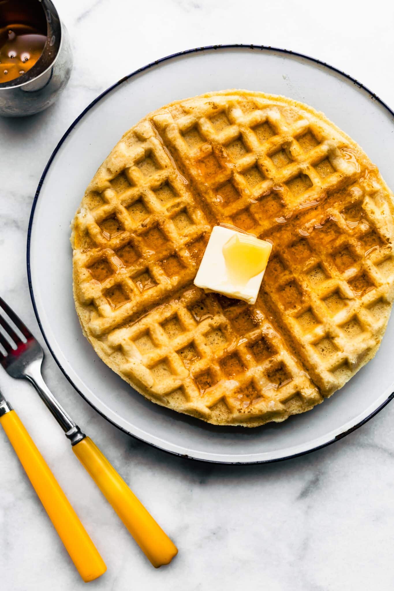 Overhead photo of a gluten free waffle on a plate topped with butter and syrup.