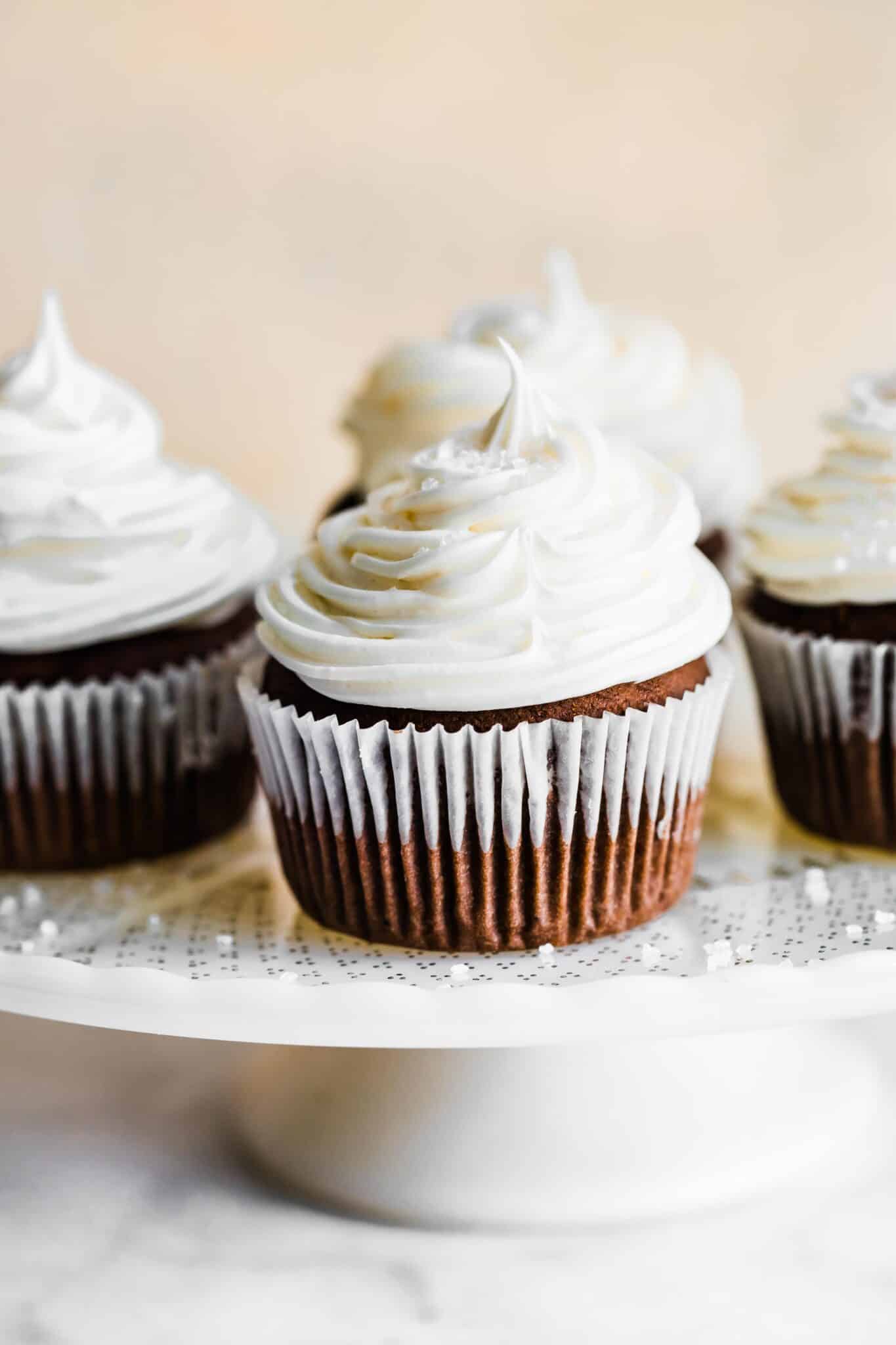 Gluten free chocolate cupcakes topped with cream cheese frosting on a white cake plate.