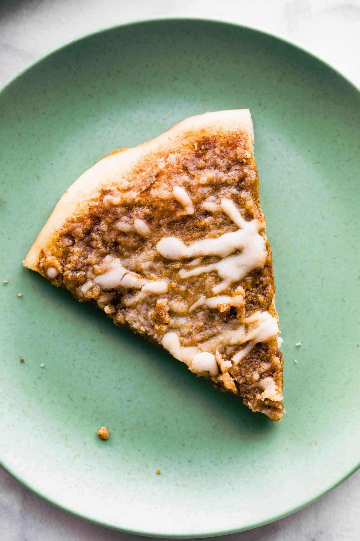 Overhead photo of a slice of cinnamon dessert pizza on a green plate.