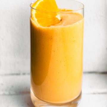 Up close photo of an orange carrot smoothie with an orange slice on top.