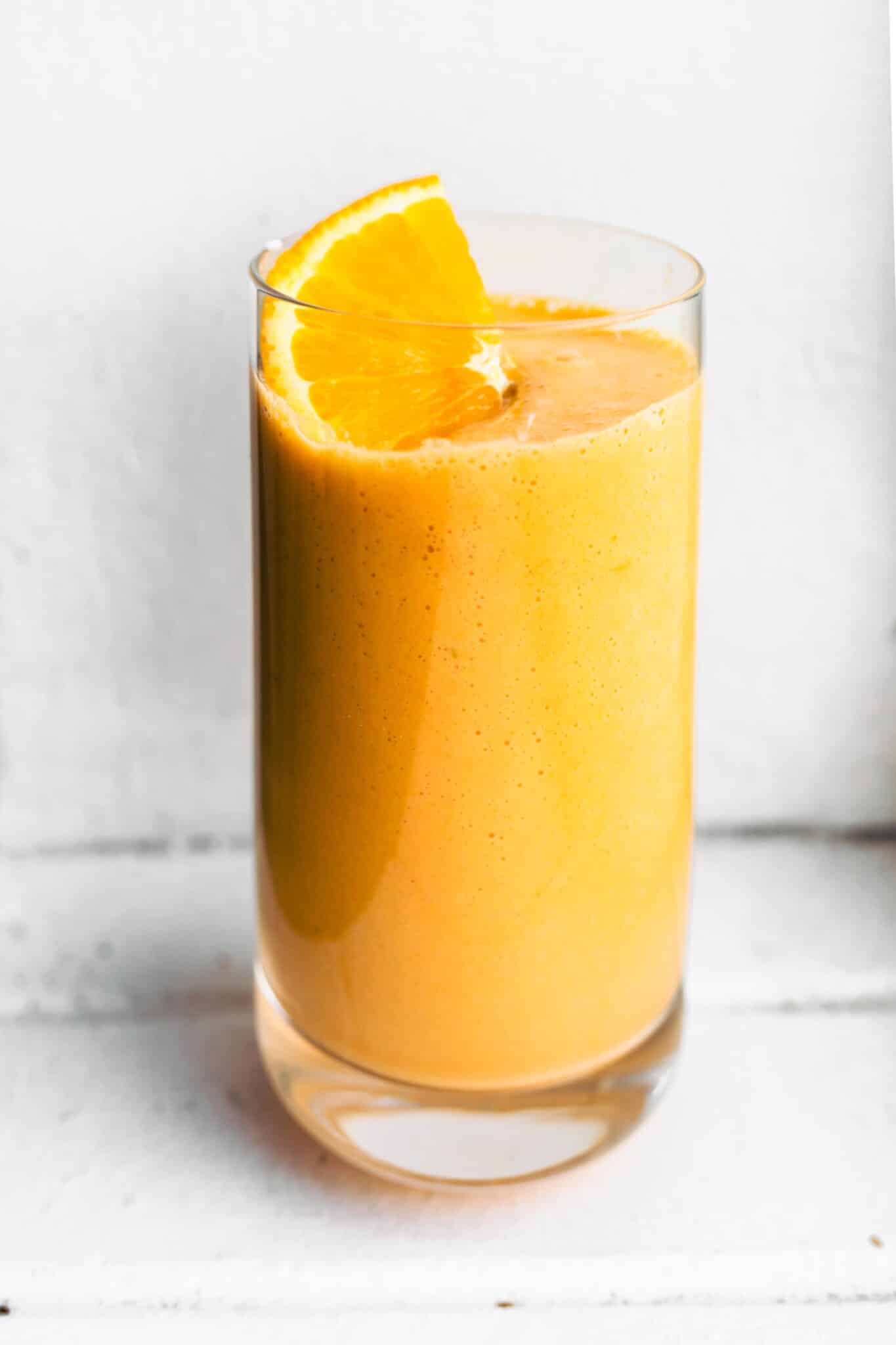 Up close photo of an orange carrot smoothie with an orange slice on top.