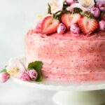 Up close photo of a gluten free strawberry cake topped with fresh flowers and strawberries.
