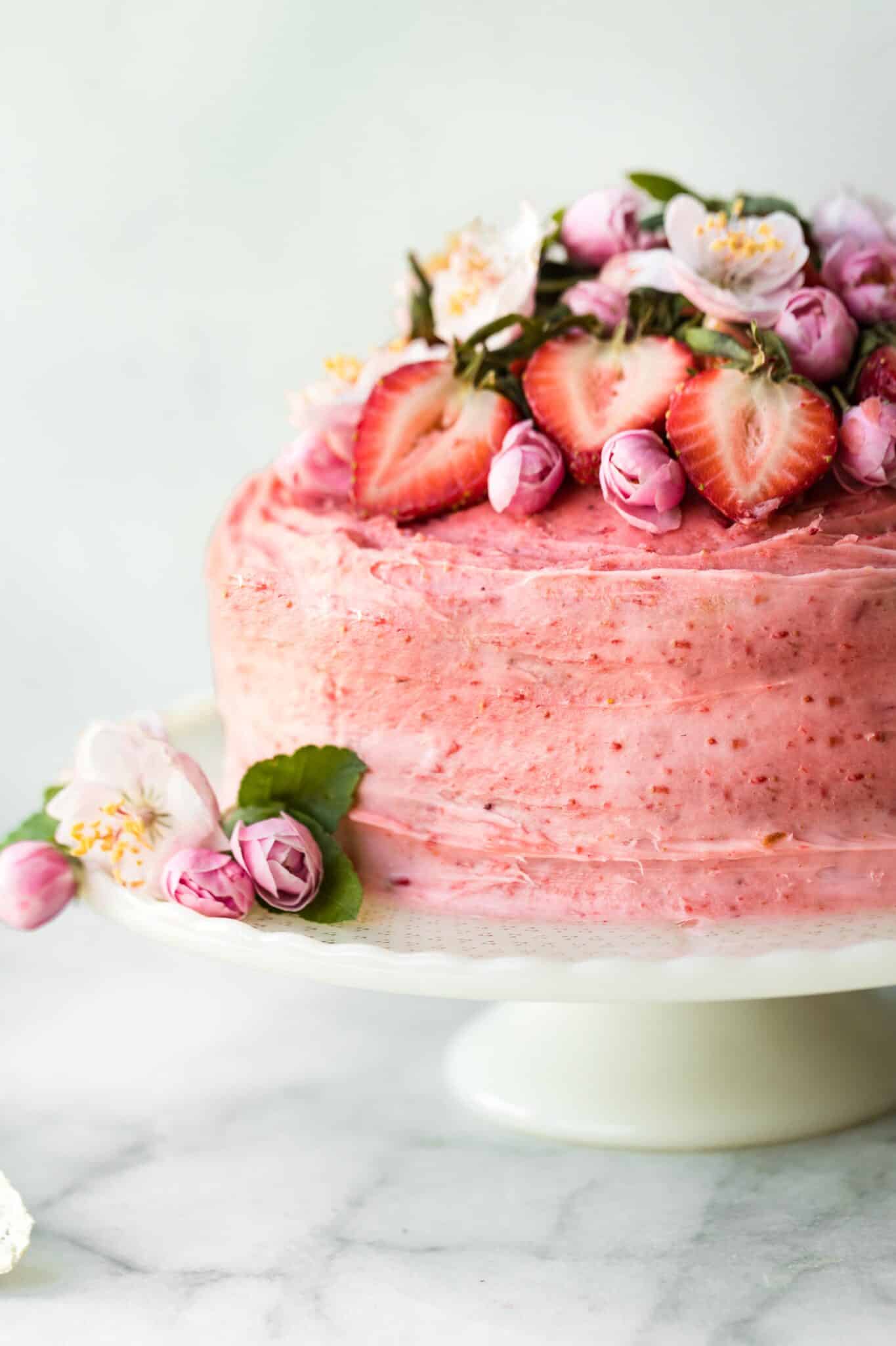 Up close photo of a gluten free strawberry cake topped with fresh flowers and strawberries.