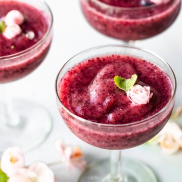 Three glasses of frozen wine slushies topped with pink flowers.