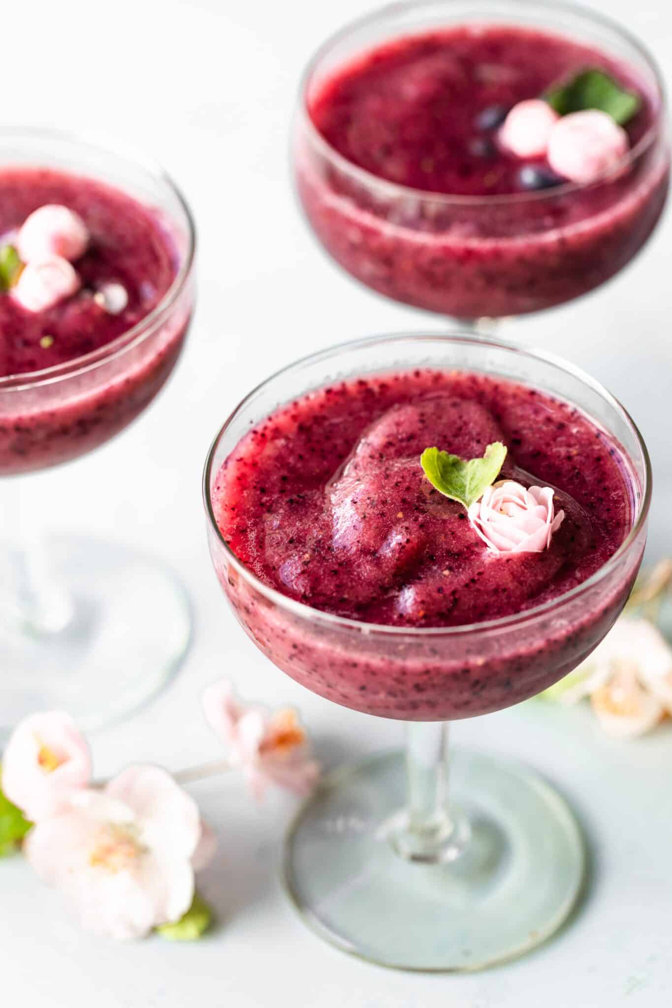 Three glasses of frozen wine slushies topped with pink flowers.
