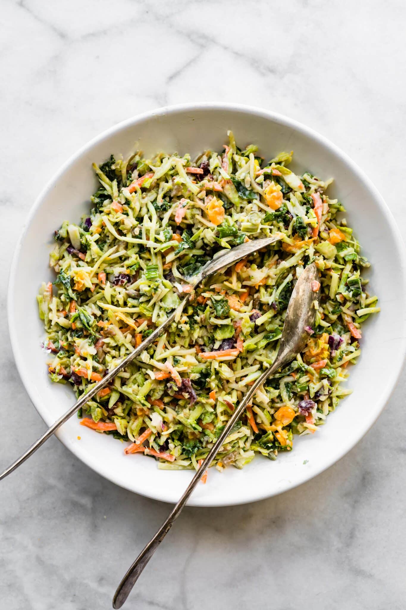 Overhead photo of a healthy broccoli slaw in a white bowl with two spoons.