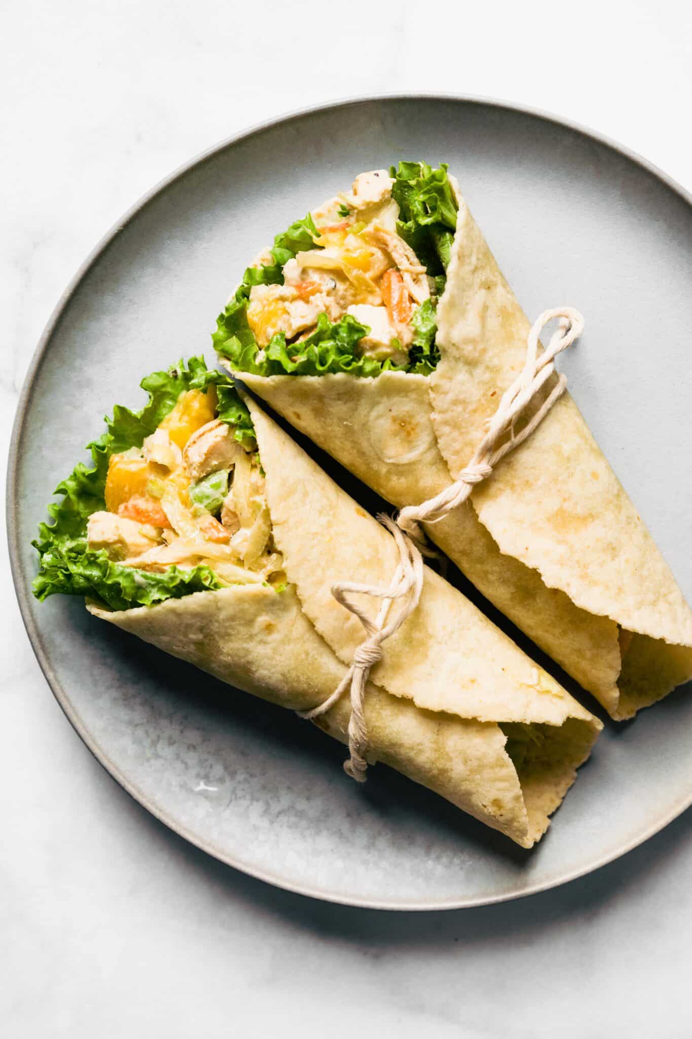 Photo of two Asian chicken salad wraps on a plate tied closed with a string.