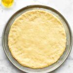 No yeast pizza dough on a metal sheet pan with a jar of oil.