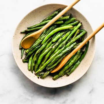 Cooked green beans in shallow bowl with two wooden spoons.