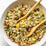Two wooden serving spoons in a bowl of pretty quinoa with veggies.