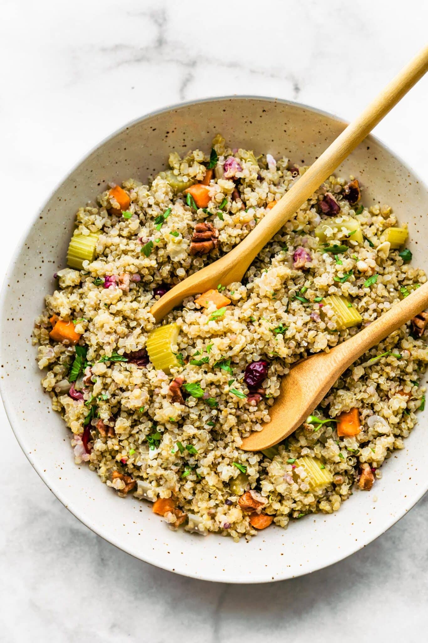 Two wooden serving spoons in a bowl of pretty quinoa with veggies.