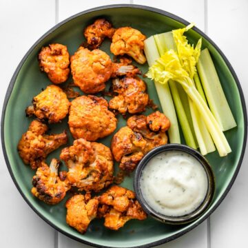 Overhead photo of vegan buffalo cauliflower in a green serving dish with celery and dip.