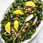 A white oval plate of goat cheese and pear kale salad with two serving spoons.