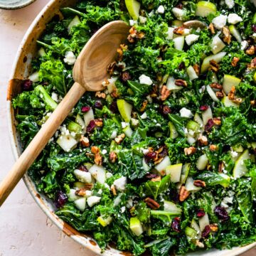 A large bowl of kale salad with a serving spoon and a bowl of pecans.
