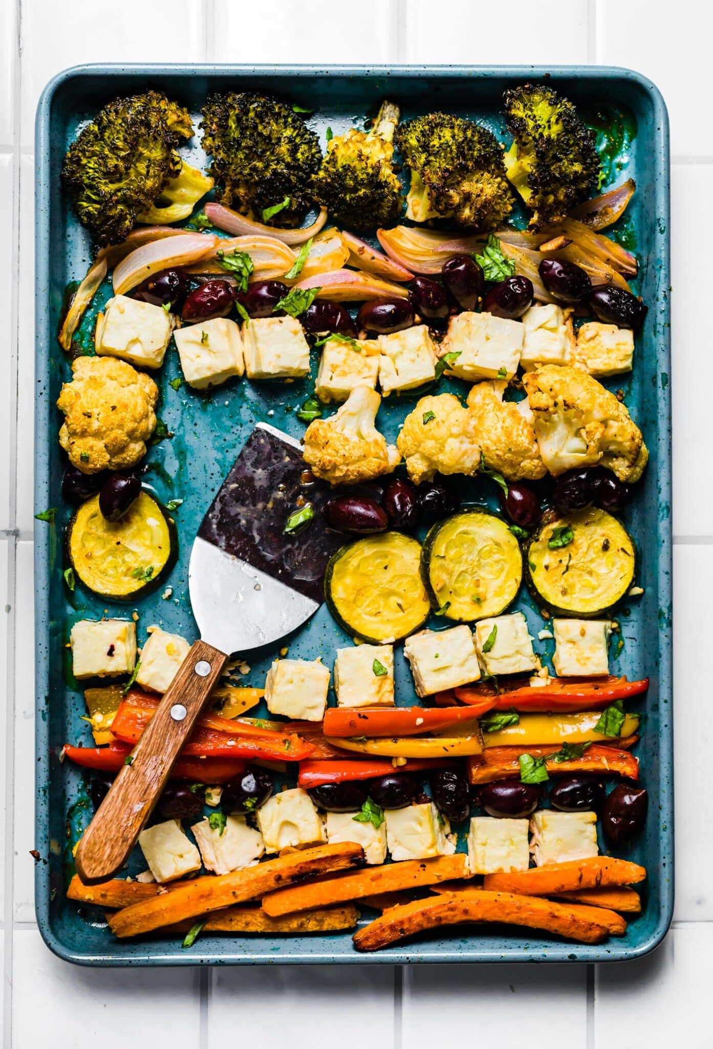 Overhead photo of baked Mediterranean vegetables on a sheet pan with a spatula.