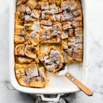 overhead photo of french toast casserole in a white rectangle dish with a slice of casserole on a serving utensil