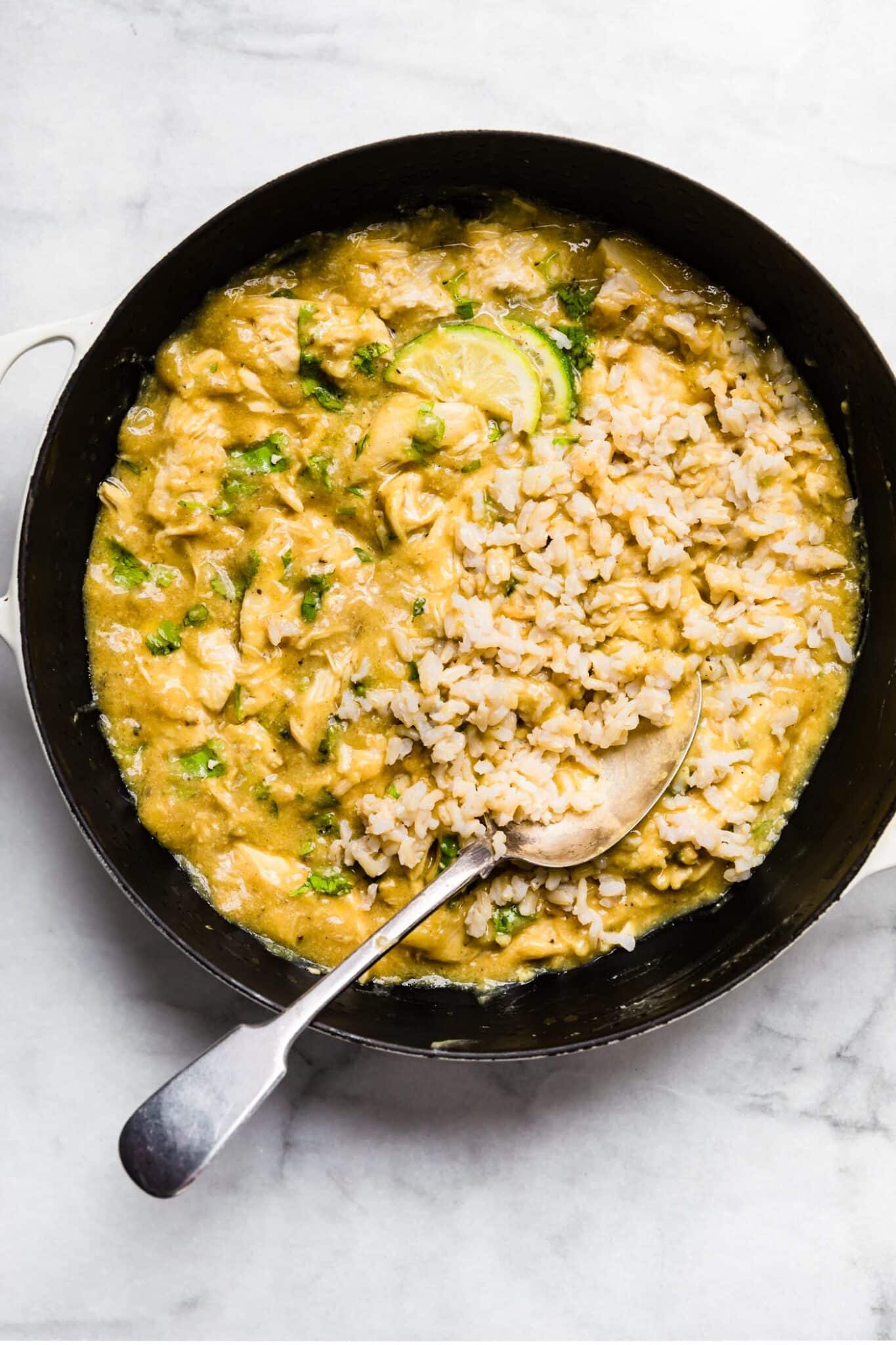 Coconut milk chicken in a cast iron pan with a spoon and rice.