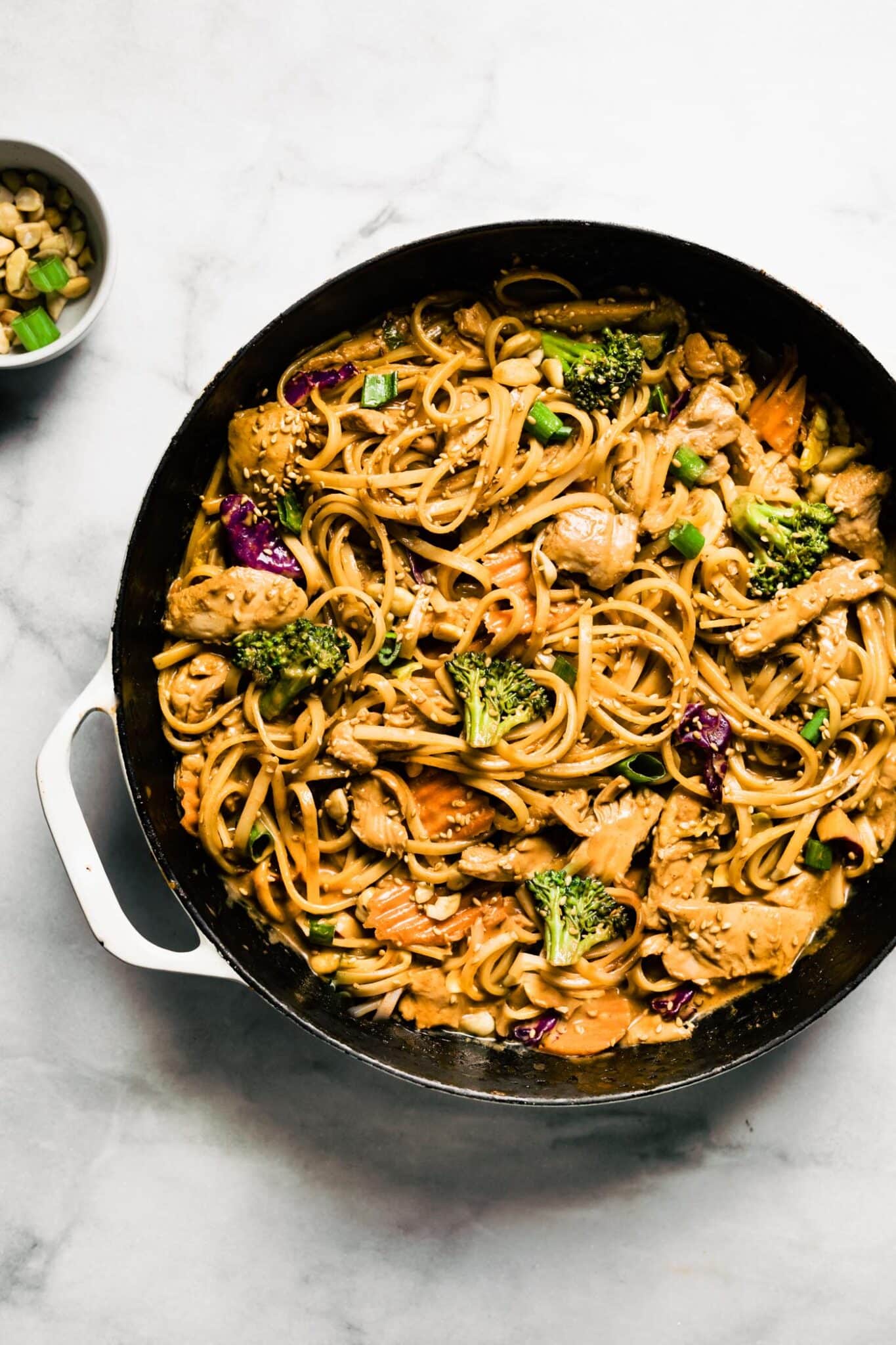 Overhead photo of one pot Thai peanut sauce noodles on a white marble countertop.