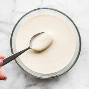 A woman placing spoon in a bowl of cashew cream sauce.