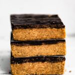 Three no bake chocolate almond flour bars stacked on a white countertop.