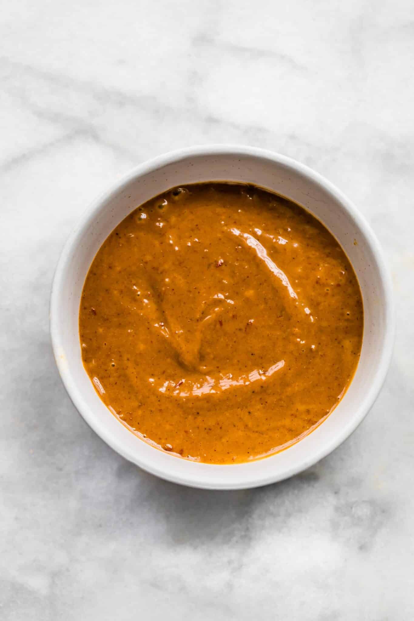 A bowl filled with thick peanut sauce on a white marble countertop.
