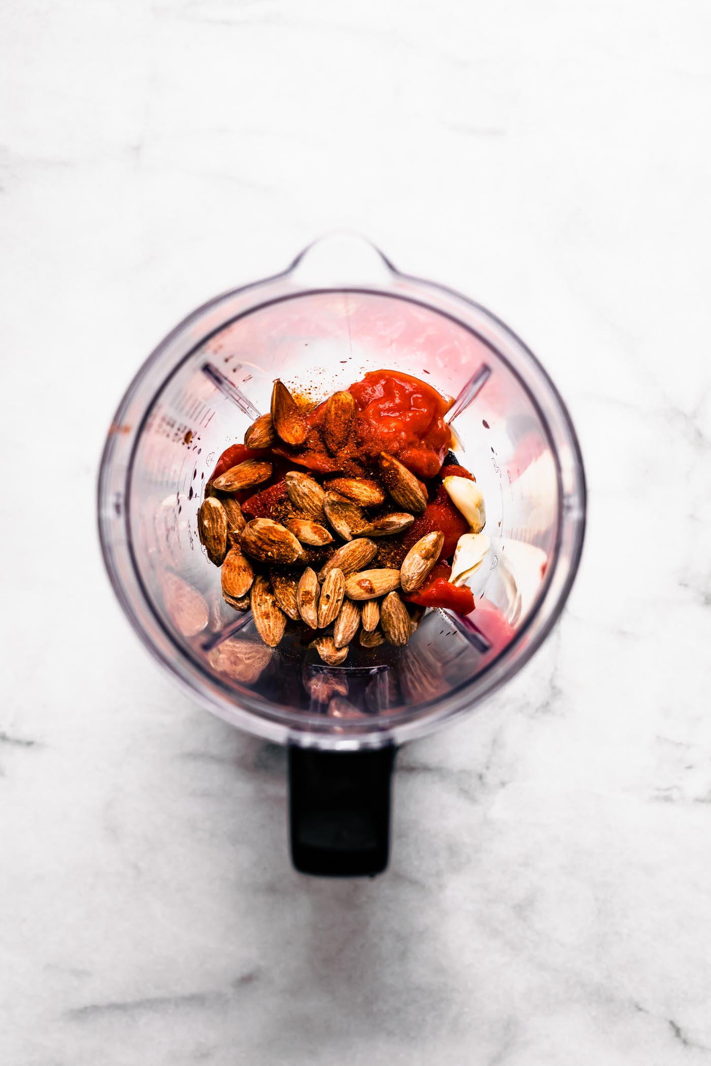over head photo of blender with ingredients to make roasted red pepper sauce. smoked nuts, red pepper, tomato, garlic