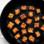 Cubed tempeh sautéed in a stovetop pan.