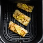 3 Cooked fish fish fillets topped with a lemon sitting in an air fryer