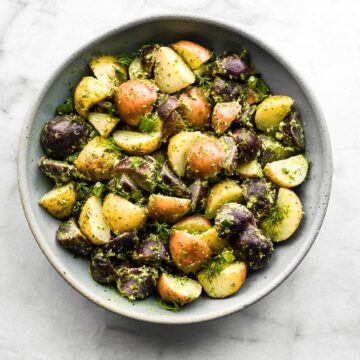 Halved baby potatoes coated in a creamy herb sauce in a bowl.
