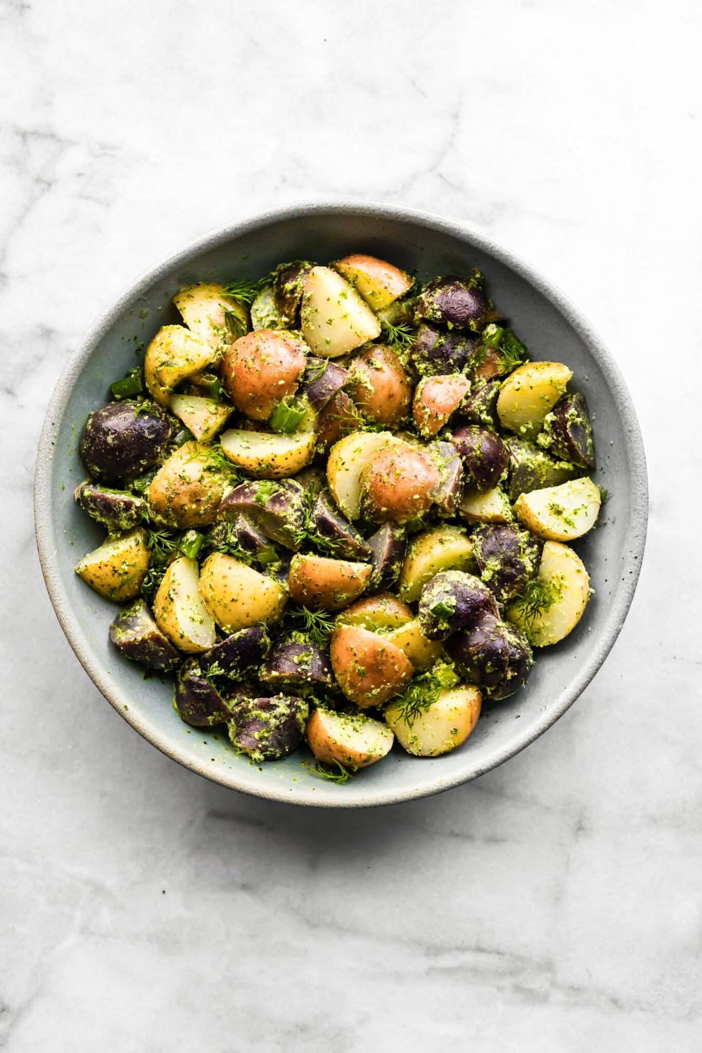 Halved baby potatoes coated in a creamy herb sauce in a bowl.