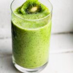 A bright green kiwi smoothie in a glass topped with a kiwi slice.