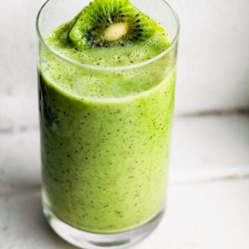 A bright green kiwi smoothie in a glass topped with a kiwi slice.