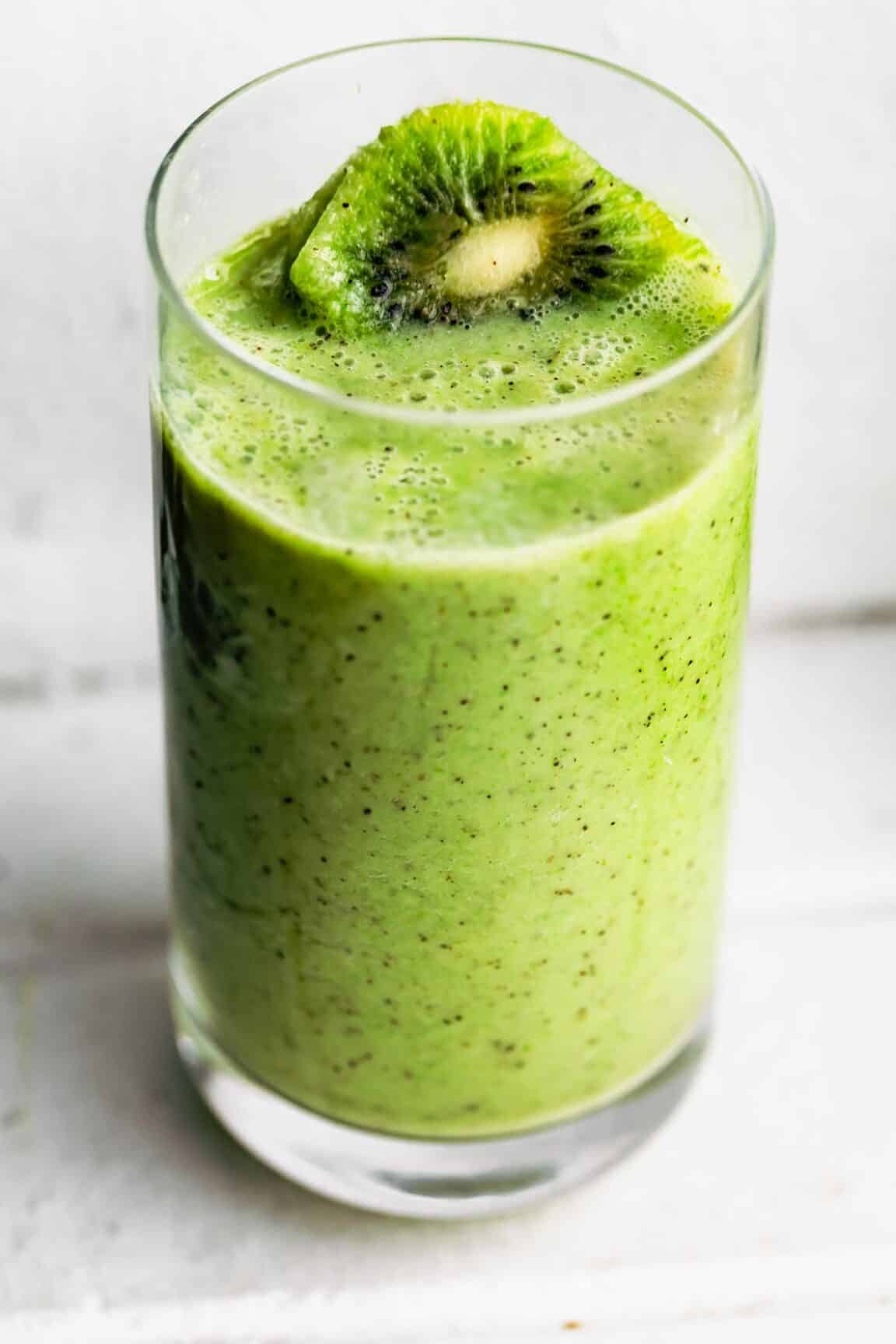 A bright green kiwi smoothie in a glass topped with a kiwi slice.