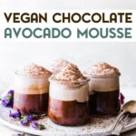 A photo of 4 small glass jars of vegan chocolate avocado mousse sitting on a plate with 2 spoon with a text overlay for pinterest.