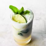 A glass filled with creamy coconut mojito topped with fresh mint leaves and lime slice.
