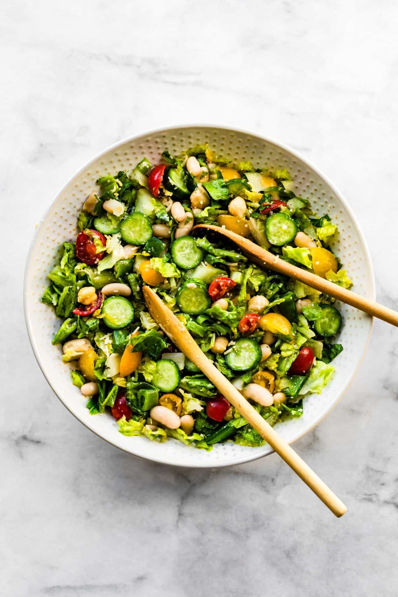 white bowl filled with chopped romaine salad with wood serving spoons in it.