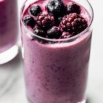 Tall glass filled with a purple smoothie, topped with berries