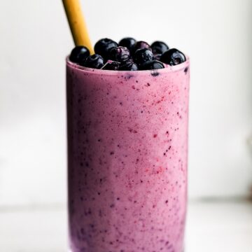 Tall glass filled with a purple smoothie, topped with berries and a straw.