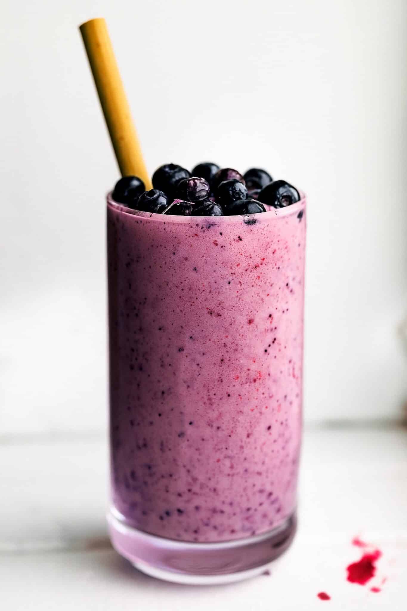 Tall glass filled with a purple smoothie, topped with berries and a straw.