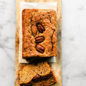 overhead photo of partially sliced zucchini bread with walnuts on top on a wood plank