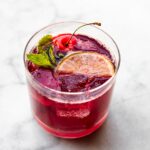 overhead photo of a Clear glass of tart cherry drink garnished with a lime, cherry, and fresh mint.